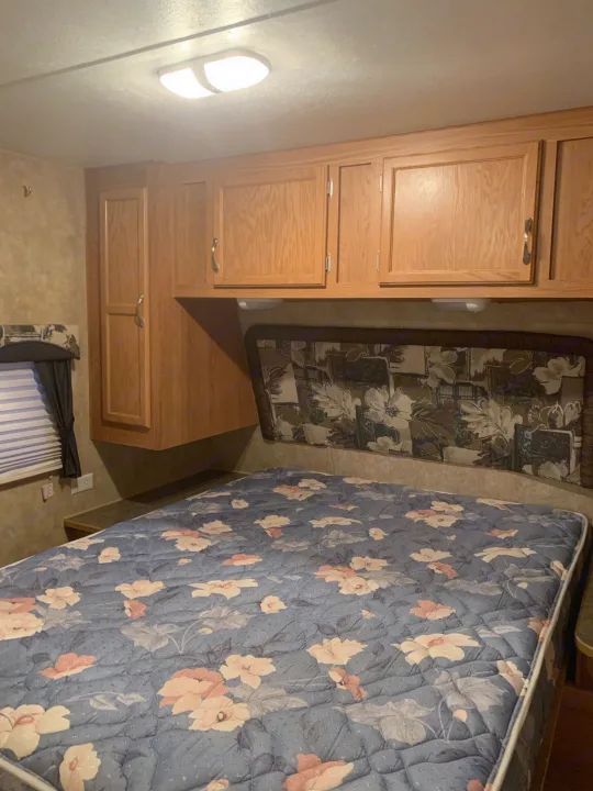 Cozy RV rental bedroom features a floral bed, wooden cabinets, and a window. Perfect for a camper's retreat.. Jayco Jay Flight 2007