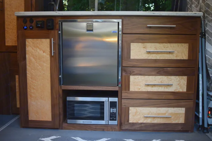 Inside an RV rental: a modern galley with custom walnut & maple burl cabinetry, stainless fridge, microwave, and power panel.. Mercedes-Benz Sprinter 2016