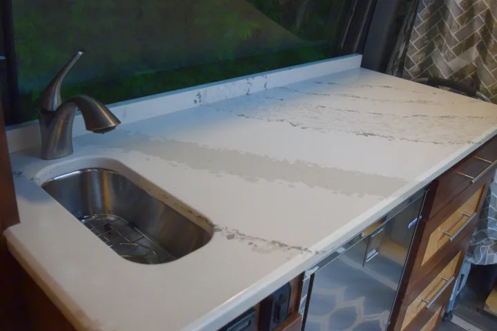 Compact RV rental kitchen: white counter with sink, modern faucet, and visible water on its gray-patterned surface.. Mercedes-Benz Sprinter 2016