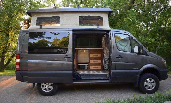 This gray Mercedes Sprinter camper van, ideal for RV rental, features a pop-top roof and an organized interior kitchen.. Mercedes-Benz Sprinter 2016