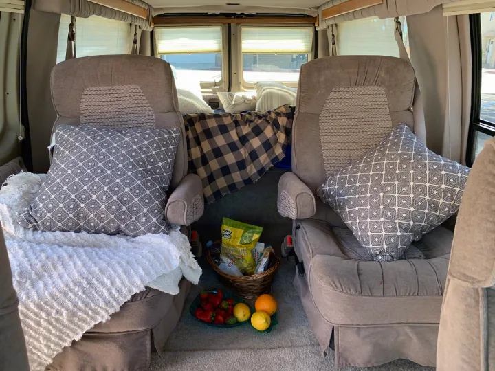 Cozy RV rental interior with two comfy seats, patterned cushions, a warm blanket, and fresh fruit for a pleasant journey.. Ford Econoline 150 2004