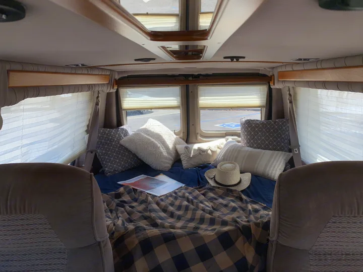 Cozy camper van RV rental interior: bed with pillows, plaid blanket, hat, and magazine. Perfect for travel!. Ford Econoline 150 2004