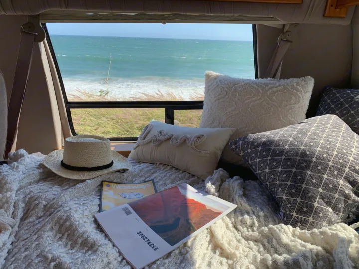 Relaxing RV rental interior with a stunning ocean view, soft pillows, & blanket. Ideal for cozy van travel.. Ford Econoline 150 2004