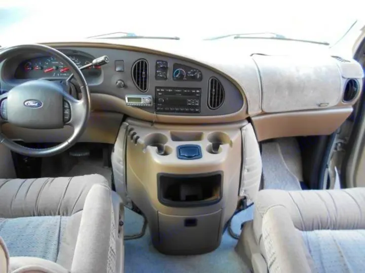 Inside an RV rental: detailed view of the front cabin, dashboard, steering wheel, and passenger seats.. Ford Econoline 150 2004