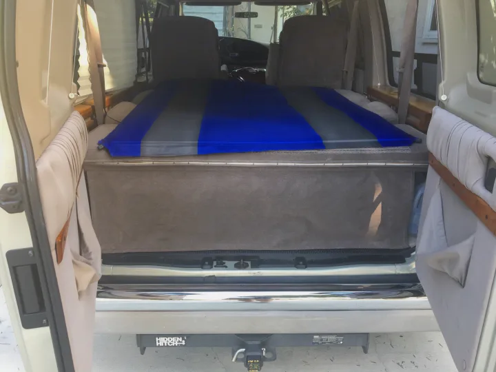 RV rental camper van interior from the rear, featuring a blue and grey inflatable mattress bed over covered storage.. Ford Econoline 150 2004