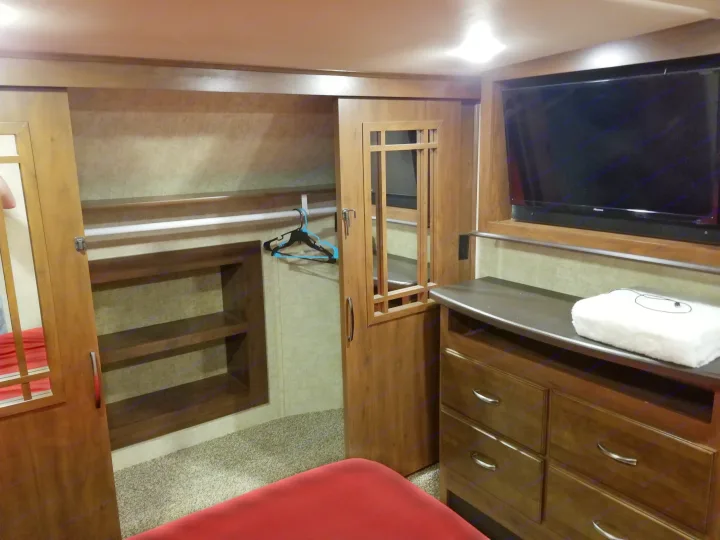 RV rental bedroom showcasing built-in storage: TV, dresser, and a closet with a hanging rod & shelves.. Forest River Sierra 2018