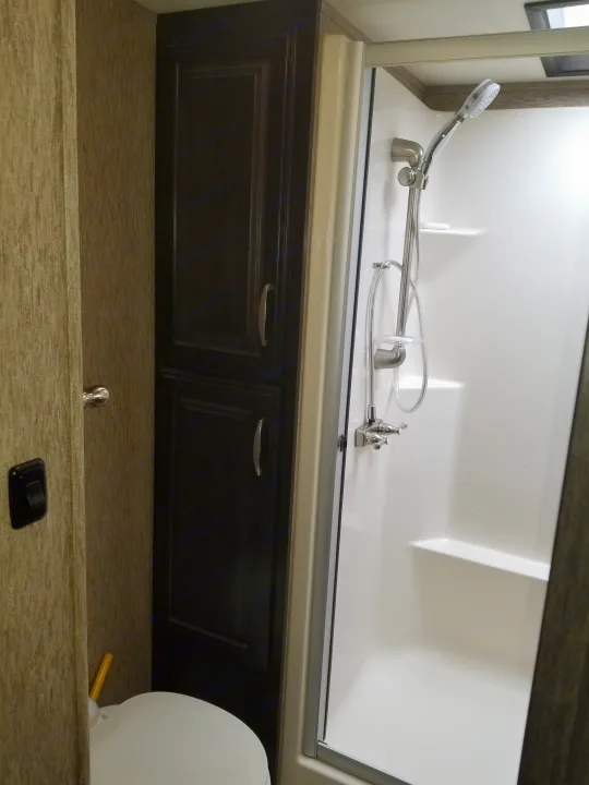 RV rental bathroom: white shower stall, toilet, and dark wood storage cabinet visible.. Grand Design Momentum 385 TH 2015