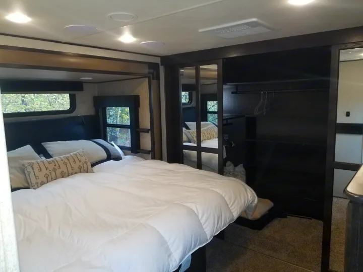 Step into comfort with this RV rental bedroom, featuring a cozy bed, mirrored closet, and scenic window views.. Grand Design Momentum 385 TH 2015