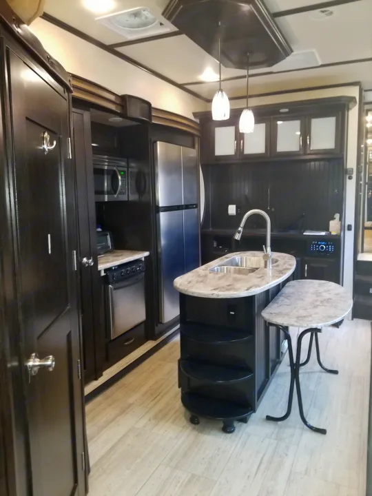 Spacious RV rental kitchen with dark wood cabinets, island sink, refrigerator, and oven, ready for your next adventure.. Grand Design Momentum 385 TH 2015