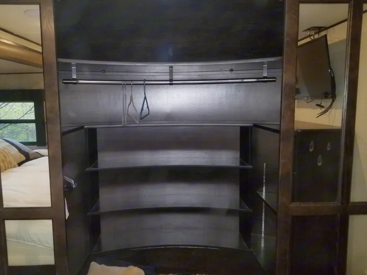 An RV rental's built-in wardrobe with a hanging rod, multiple shelves, and mirrored doors reflecting the bedroom area.. Grand Design Momentum 385 TH 2015