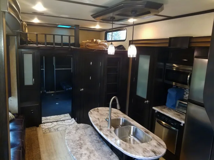 Spacious rv rental interior featuring a modern kitchen island, living area, and bunk beds. Dark wood accents and light countertops create a contemporary feel.. Grand Design Momentum 385 TH 2015