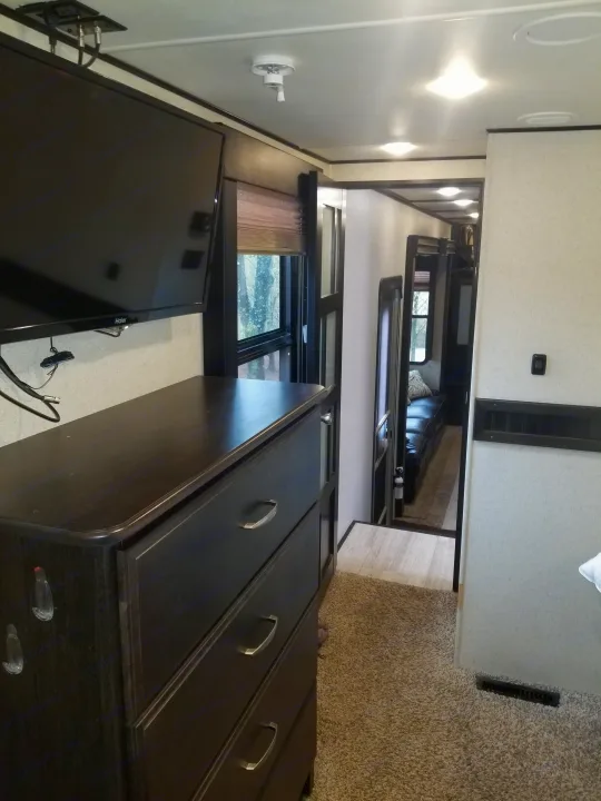 Bright RV rental interior featuring a TV, dresser, and a hallway leading to a comfortable lounge area.. Grand Design Momentum 385 TH 2015