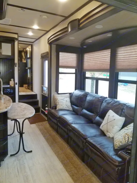 Spacious, modern RV living area with a dark leather sofa, bay windows, and light flooring. Ideal for your next RV rental.. Grand Design Momentum 385 TH 2015