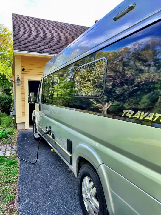 Light green Travato RV rental van charging in a driveway next to a yellow house. Ready for travel!. Winnebago Travato 2019