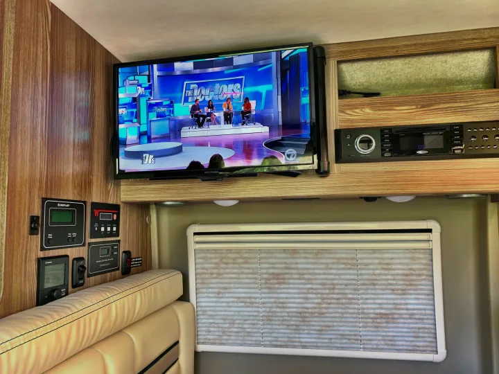 RV rental: Interior view with TV playing "The Doctors," control panels, and entertainment system above seating and a window.. Winnebago Travato 2019