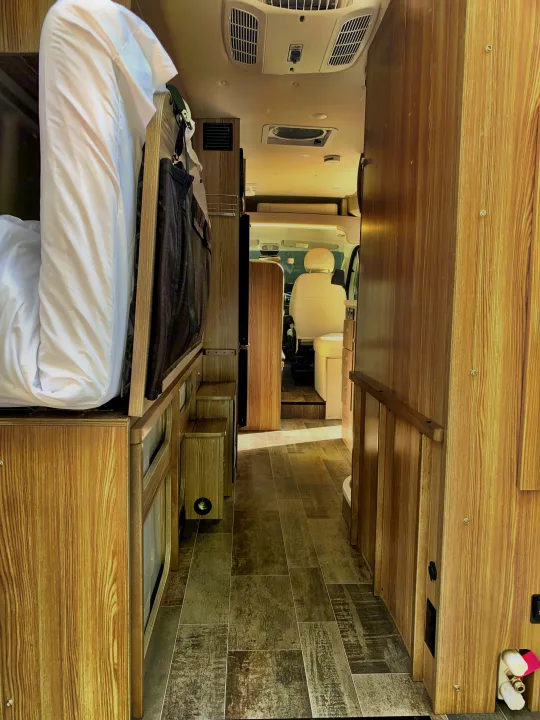 RV rental interior looking forward: bed on left, cabinetry on right, leading to the driver's cabin.. Winnebago Travato 2019