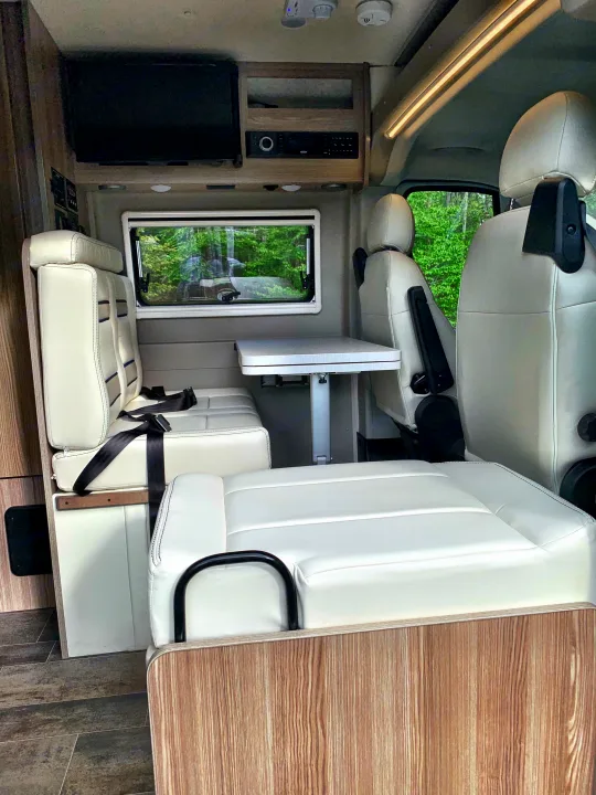 An RV rental's versatile interior featuring light leatherette seating, a convertible dinette table, and entertainment unit.. Winnebago Travato 2019