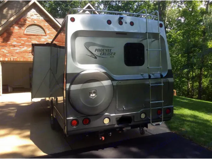 Rear view of a silver Phoenix Cruiser motorhome with extended slide-out and ladder, parked on a driveway. Great rv rental option.. Phoenix USA Cruiser 2552 2011