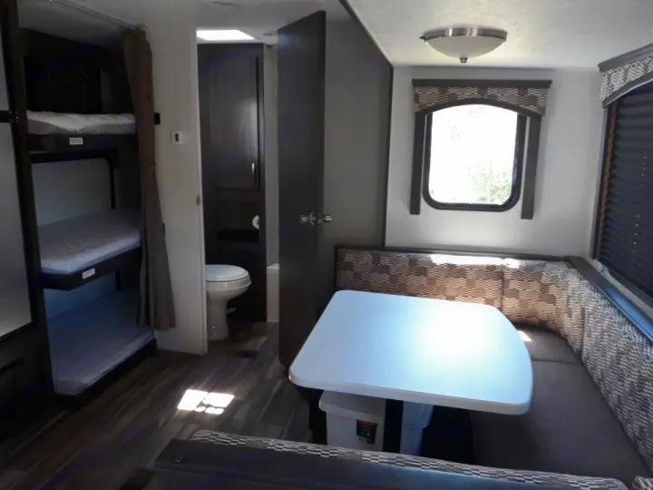 This RV rental interior features dark wood bunk beds, a white toilet in the restroom, and a U-shaped dinette.. Forest River Evo T2550 2019