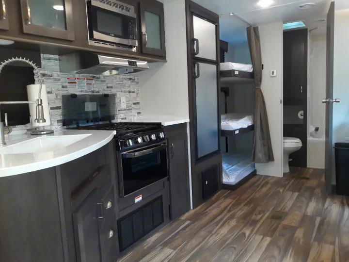 Spacious rv rental interior featuring a modern kitchen with microwave, oven, sink, and comfortable bunk beds and bathroom.. Forest River Evo T2550 2019