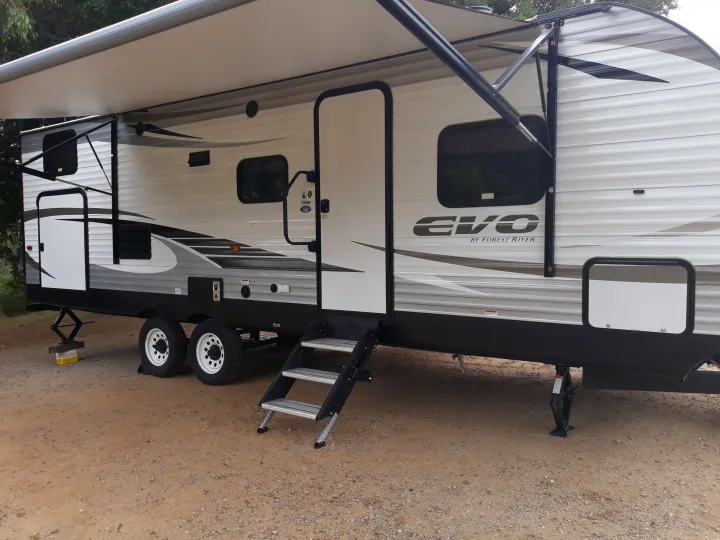 This RV rental, an EVO travel trailer with an extended awning and steps, is set up on a dirt campsite.. Forest River Evo T2550 2019