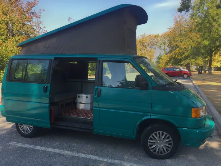 Teal pop-top camper van with open sliding door showing interior, parked in an autumn setting. Ideal as an RV rental.. Volkswagen Westfalia 1992