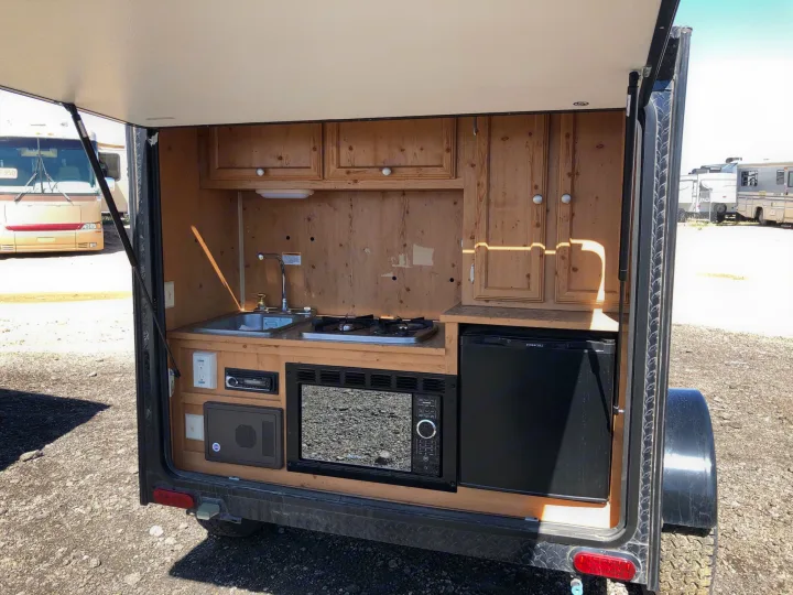 Open hatch of an RV rental revealing a compact mobile kitchen with sink, two-burner stove, microwave, and mini-fridge.. Sunset Park & Rv Inc. Other 2017