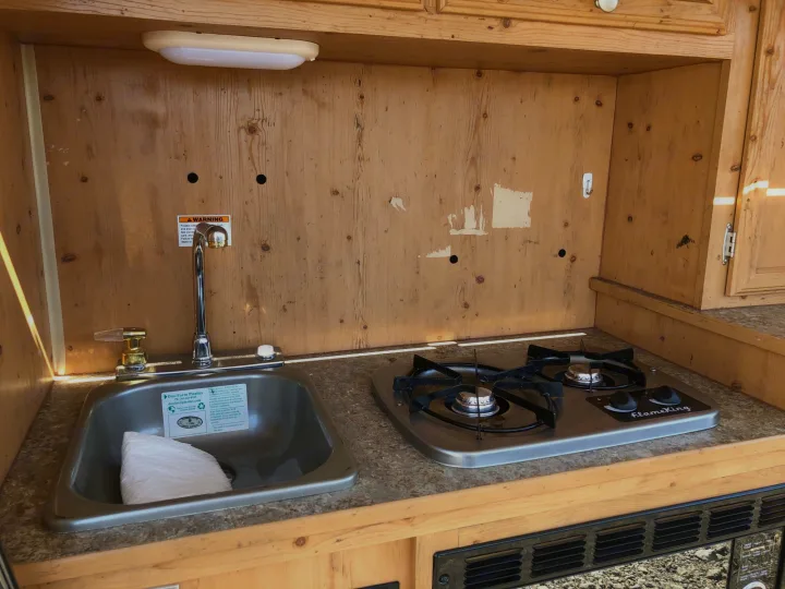 RV rental kitchenette featuring a stainless steel sink with faucet and a two-burner FlameKing stove on the countertop.. Sunset Park & Rv Inc. Other 2017