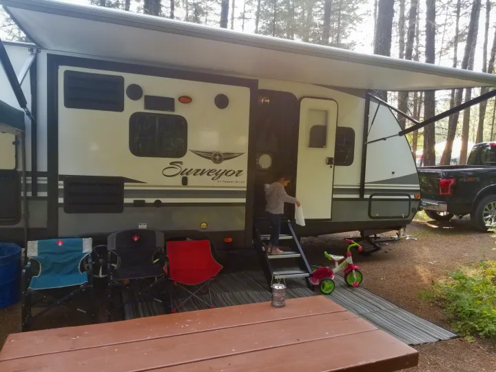 This RV rental is a Forest River Surveyor travel trailer, set up in a campground. A young girl is stepping out.. Forest River Surveyor 2019