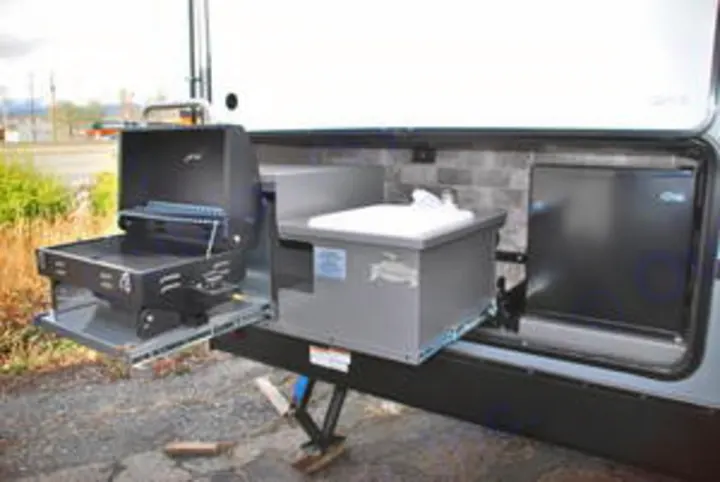 This RV's outdoor kitchen, ideal for rv rental, features a pull-out grill, sink, and mini-fridge, perfect for camp cooking convenience.. Forest River Surveyor 2019