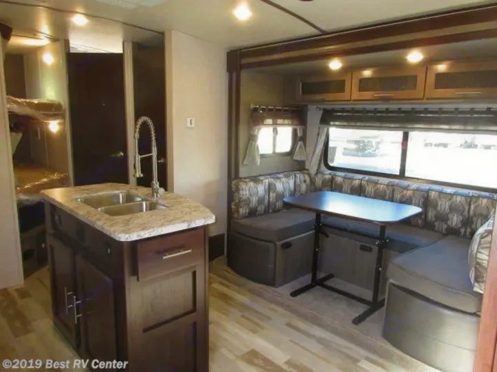 Spacious RV rental interior featuring a kitchen island with sink, U-shaped dinette, and bunk beds, ideal for travel.. Forest River Surveyor 2019