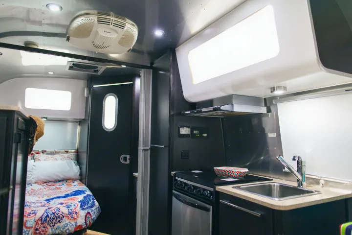 Modern RV rental interior: a compact kitchen with stove, sink, and an inviting bedroom with colorful bedding and AC.. Airstream 19 Bambi International 2012
