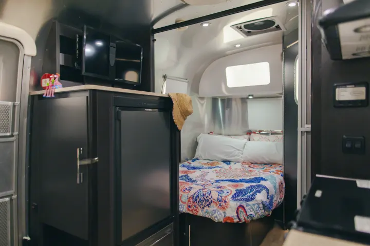 Cozy RV rental interior featuring a comfy bed with colorful bedding, entertainment TVs, and a compact kitchen.. Airstream 19 Bambi International 2012