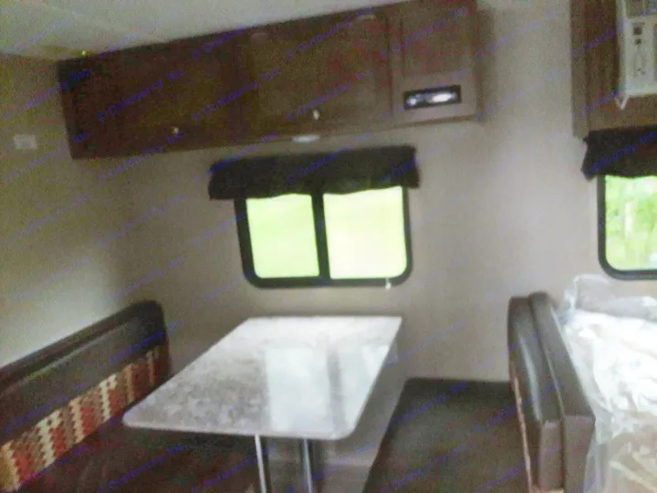RV rental interior shows a dinette with table & seating. Overhead cabinets & windows revealing green foliage outside.. Keystone ASPEN TRAIL 1700 2016