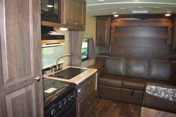 Spacious RV rental interior: modern kitchen with stove, sink, microwave, and a comfy brown sofa with an overhead bed.. Forest River Rockwood Mini Lite 2017