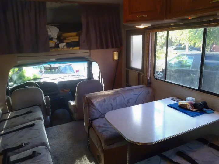 Cozy rv rental interior with dining area, driver's cabin, and a glimpse of the outdoor campground setting.. Jayco Eagle 1996