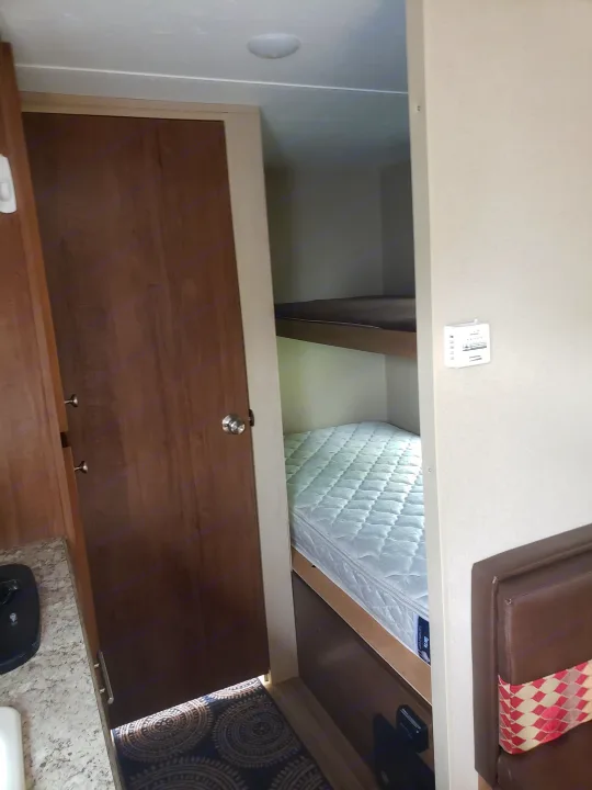 Compact RV rental interior featuring bunk beds, a small kitchen area, and dinette seating. Perfect for family adventures.. Keystone ASPEN TRAIL 1700 2016