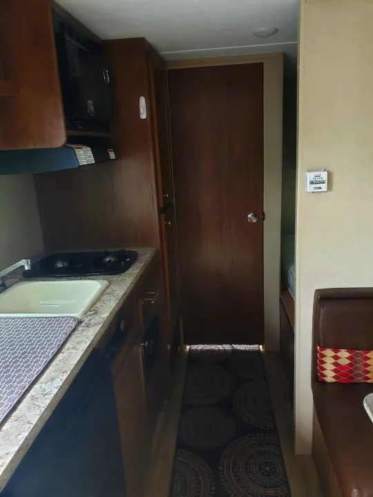 Experience comfort in our RV rental! This image shows a compact RV kitchen with a microwave, sink, and stove, leading to a cozy hallway.. Keystone ASPEN TRAIL 1700 2016