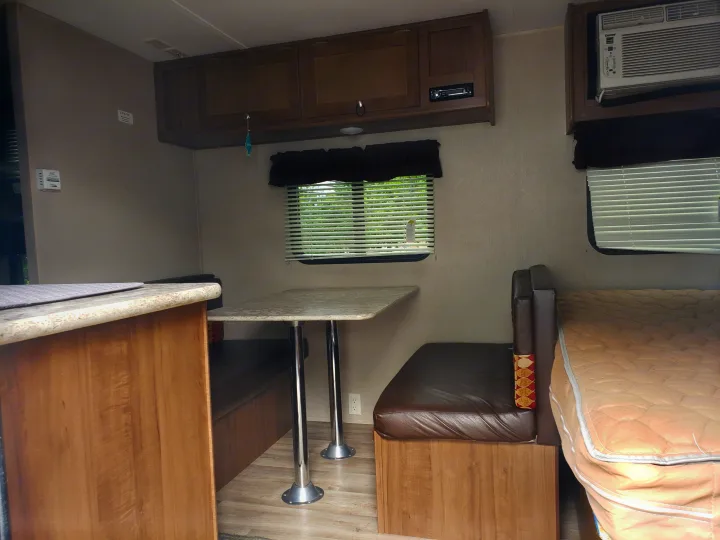 Inside an **RV rental**: a compact camper interior featuring a dinette, bed, counter, and overhead storage cabinets.. Keystone ASPEN TRAIL 1700 2016