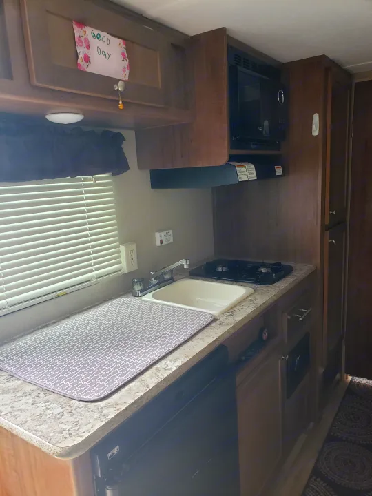 This RV rental kitchen features a sink, two-burner stove, microwave, and light wood cabinetry, making it functional and inviting.. Keystone ASPEN TRAIL 1700 2016