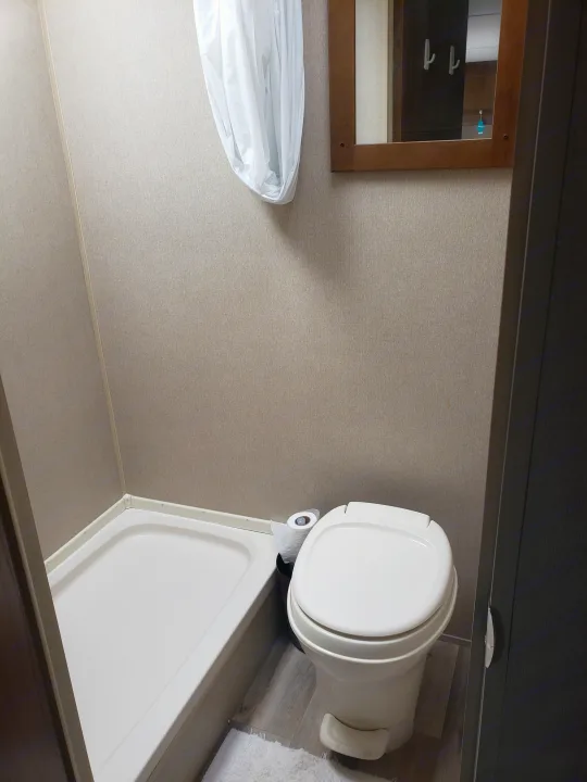 Inside an RV rental bathroom: a white shower stall, toilet with paper, and mirror. Compact and functional for road trips.. Keystone ASPEN TRAIL 1700 2016