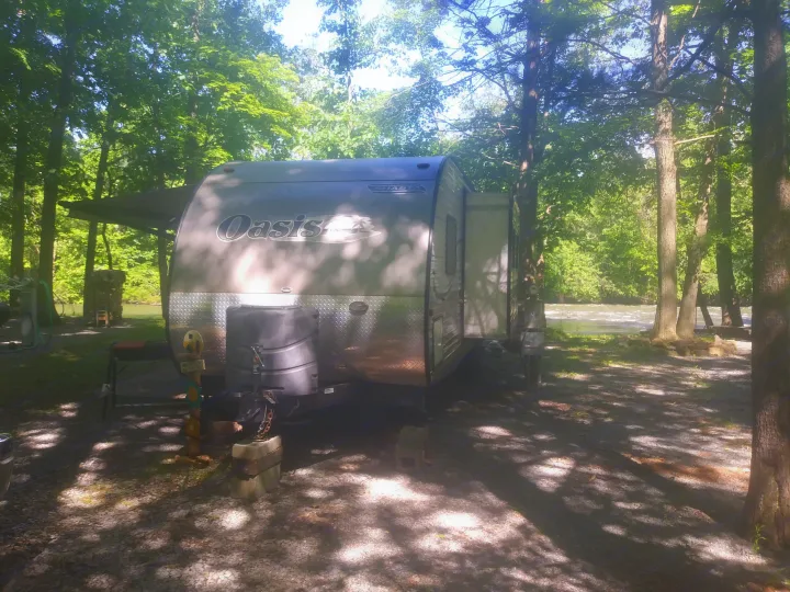 RV rental parked at a shaded, riverfront campsite amidst lush trees. Enjoy outdoor camping and nature.. Shasta Oasis 2013