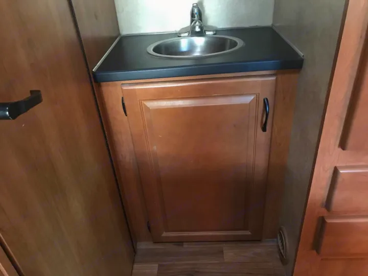 RV rental's compact bathroom vanity, featuring a stainless steel sink, faucet, and wooden storage cabinet below.. Thor Majestic 2014