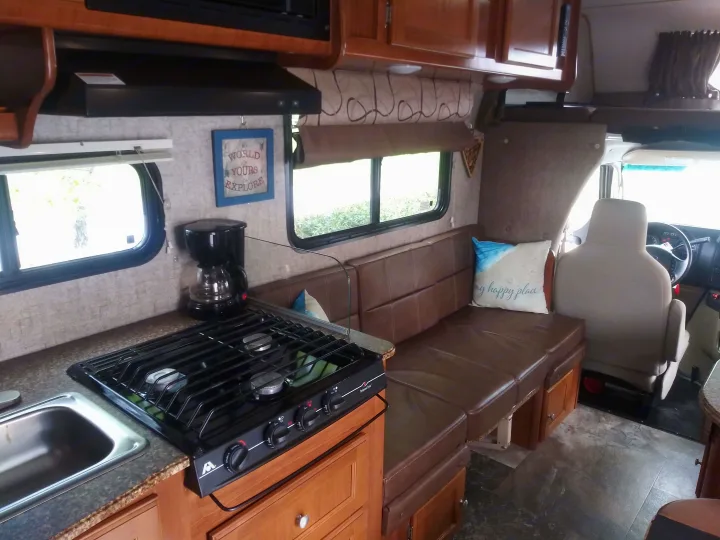 Interior front facing view features couch seating area that converts to a small table and seating for 2. (main table area seats 4 additional)  . Coachmen Leprechaun 2018