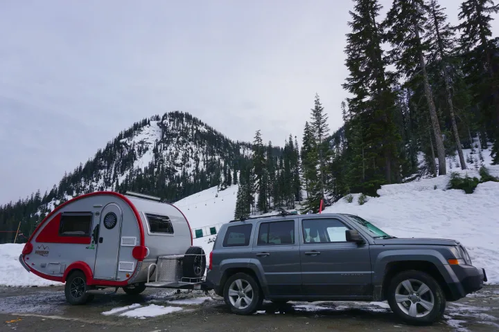 RV rental adventure: Teardrop trailer towed by Jeep in snowy mountains, surrounded by evergreen trees.. T@B Other 2019