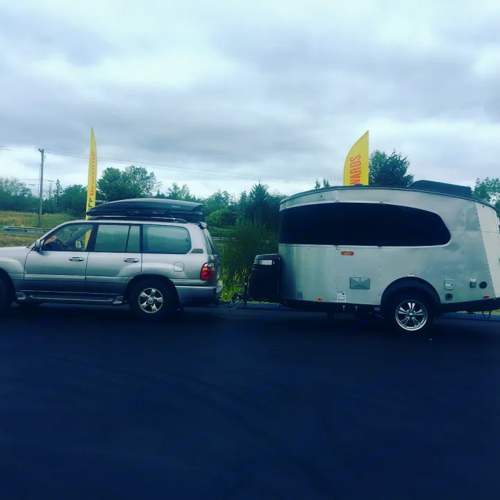 Ready for adventure! Silver SUV with roof box tows a modern travel trailer RV rental, great for camping trips.. Airstream Base Camp 2017