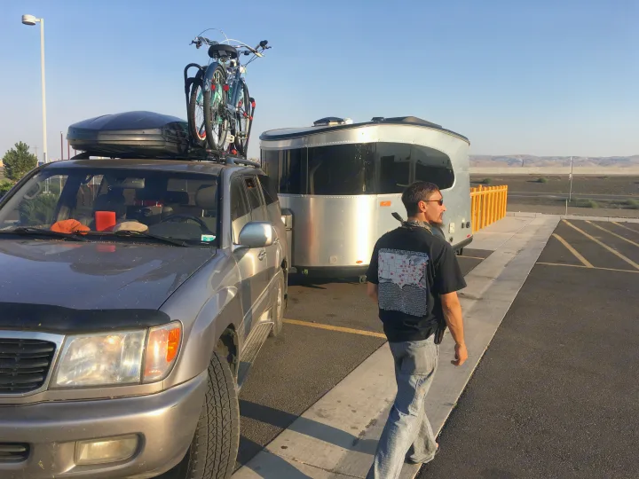 Man by his SUV, bikes on top, and an RV trailer for a road trip. Consider an RV rental for your next outdoor adventure!. Airstream Base Camp 2017