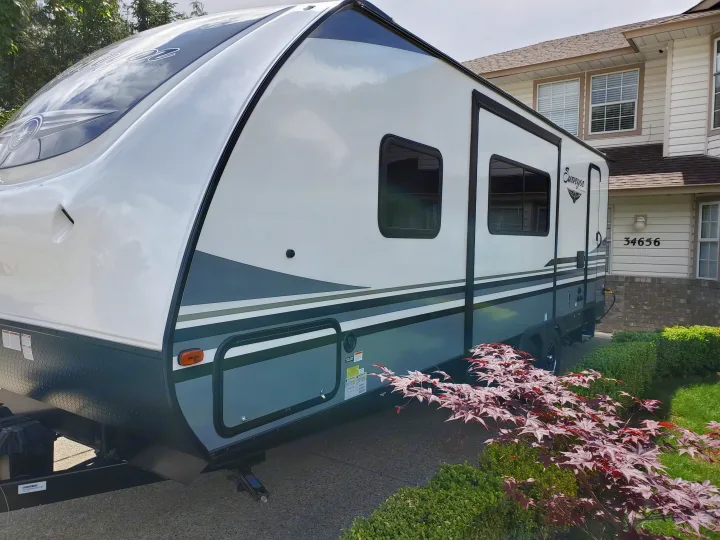 Modern white and gray Surveyor travel trailer RV, ready for rv rental adventures, parked in a residential driveway.. Forest River Surveyor 2019