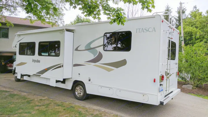 A white Itasca Impulse Class C RV rental with a slide-out extended, parked on a driveway.. Winnebago ITASCA 2009