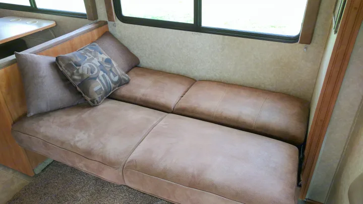Inside an RV rental: a cozy seating area with plush brown cushions, throw pillows, and large windows. Ideal for travel.. Winnebago ITASCA 2009